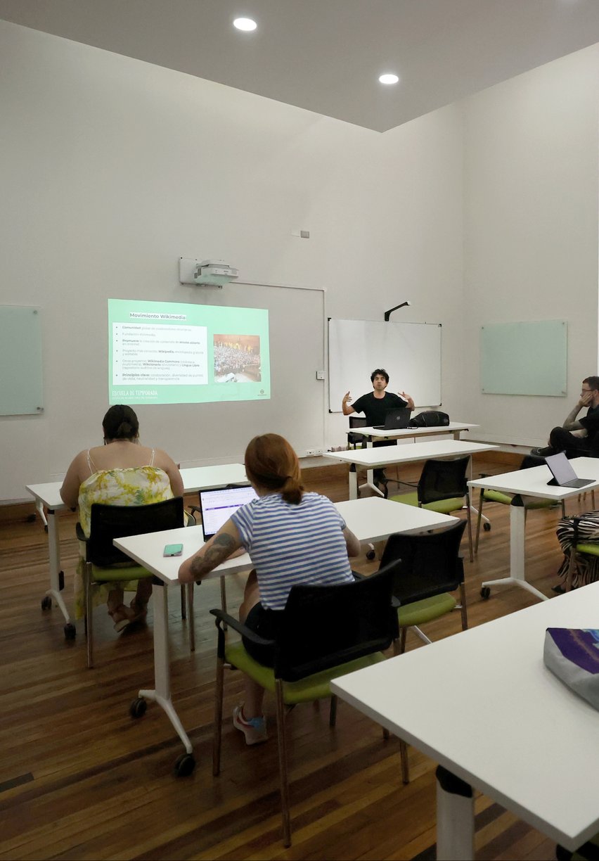 Una sala de clases con personas atendiendo una exposición.