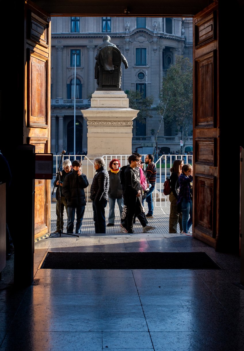 Personas en la entrada de la Casa Central, vistas desde el interior por la puerta abierta hacia la estatua de Andrés Bello.
