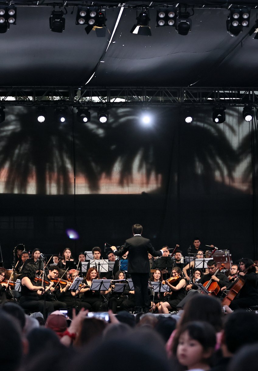 Una orquesta toca al aire libre frente a un público numeroso.